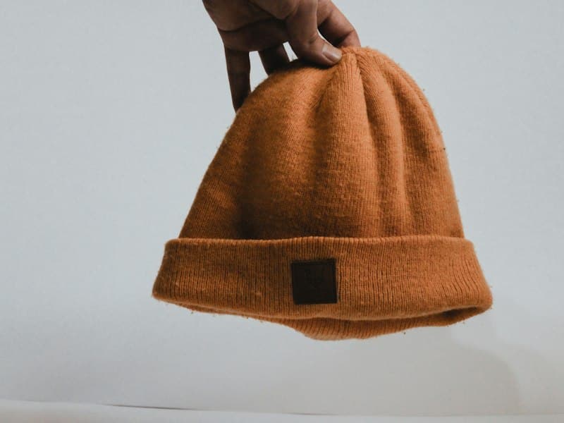 Brown knit beanie held up against a light wall